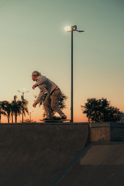 Free A skateboarder performing a trick on a ramp at sunset in a skate park. Stock Photo