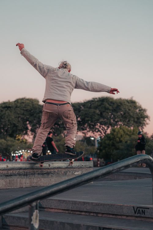 Free A skateboarder in khaki pants performs a trick on a rail at an outdoor skatepark during twilight. Stock Photo