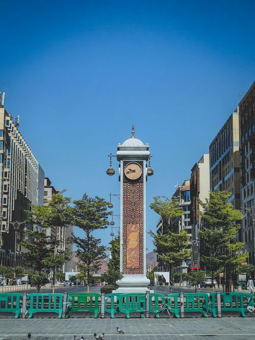 Free Urban street view with a central clock tower and tall buildings under blue sky. Stock Photo