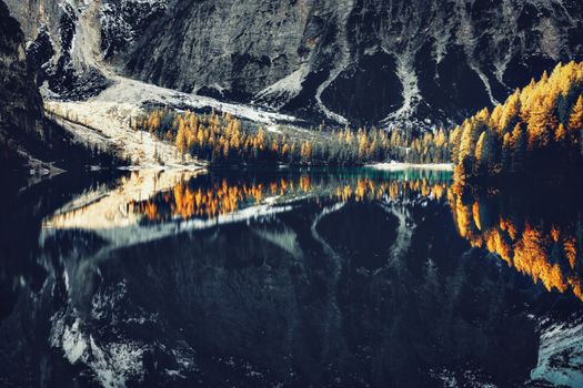 Serene lake reflecting autumn trees and majestic mountains, creating a picturesque landscape.
