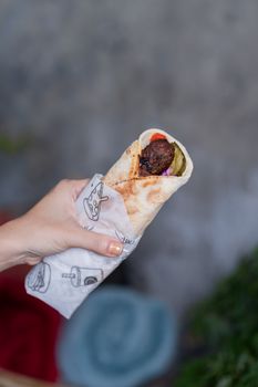 Hand holding a flavorful falafel wrap outdoors, showcasing fresh ingredients.