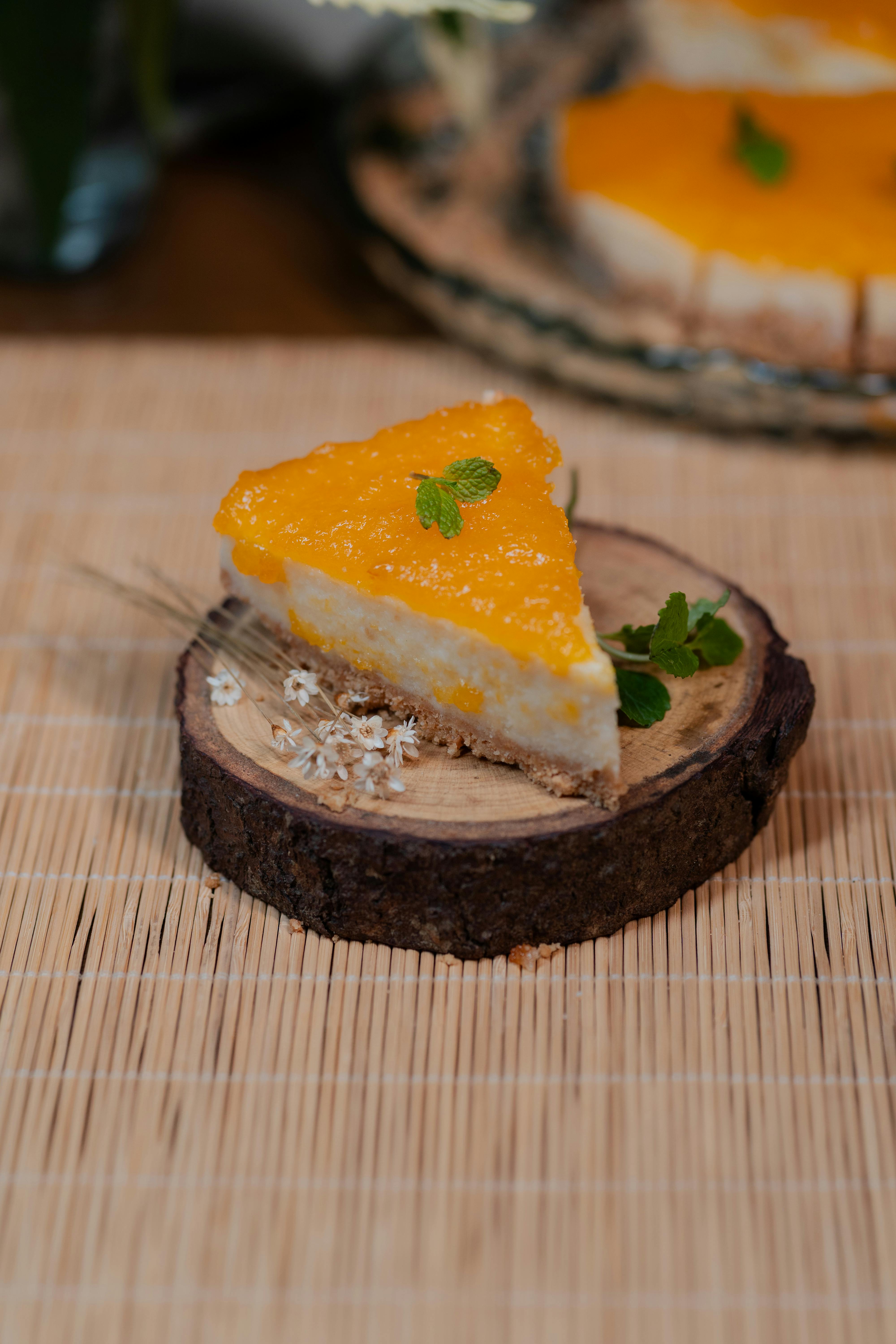 A tempting slice of mango cheesecake garnished with mint leaves, placed on a rustic wooden plate.