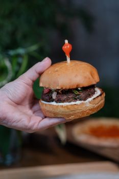 A close-up of a gourmet burger slider with a decorative red skewer, held in a hand.