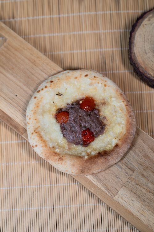 Free Mini pizza topped with olive tapenade and cherry tomatoes on a wooden board. Stock Photo