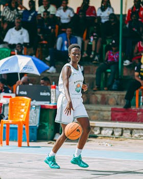 An athlete dribbling a basketball during an outdoor game, with spectators in the background.
