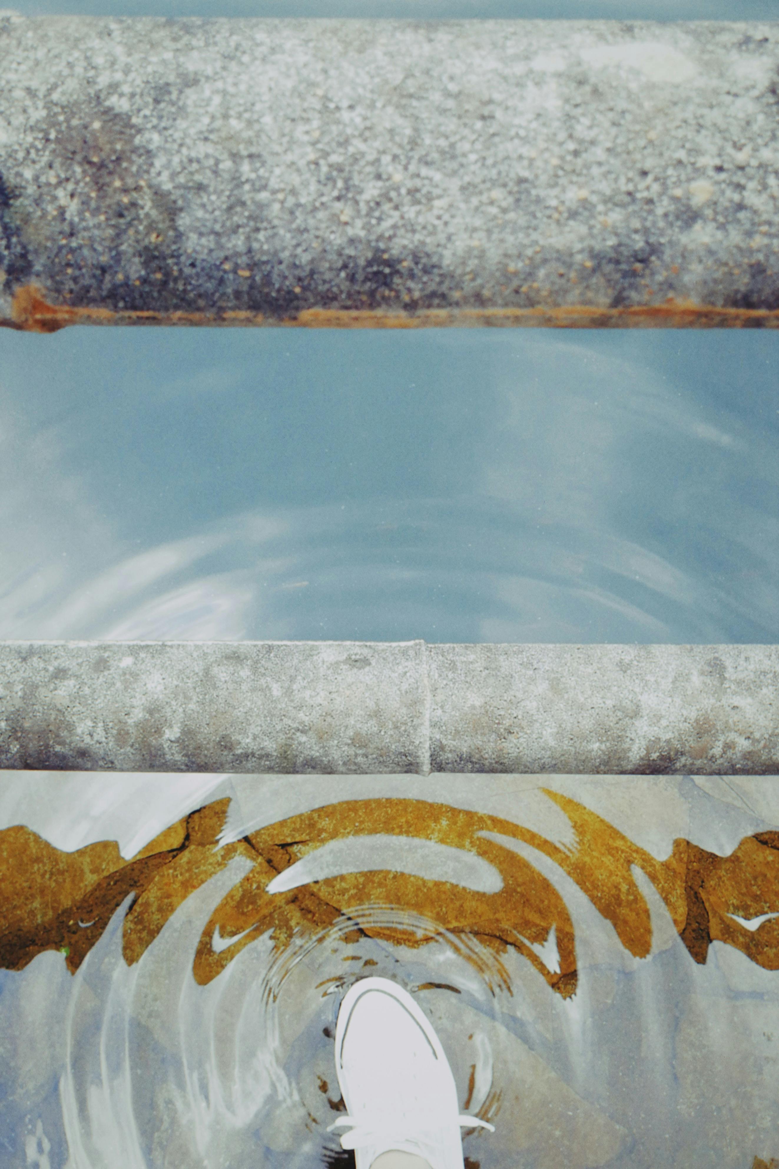 A white shoe steps into a reflective water surface creating ripples.