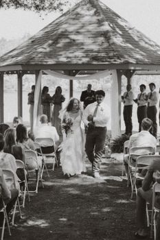 A black and white photo of a joyful couple exiting their outdoor wedding at a gazebo.