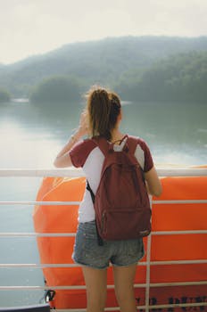 Back view of a young woman with backpack enjoying peaceful river landscape.