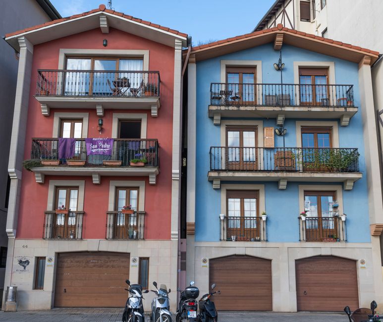 Casas adyacentes de color rojo y azul vibrantes con balcones, motos estacionadas en frente.