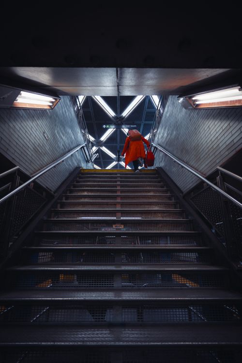 Free A person in a red coat ascends subway stairs in a New York City station, captured from a low angle. Stock Photo