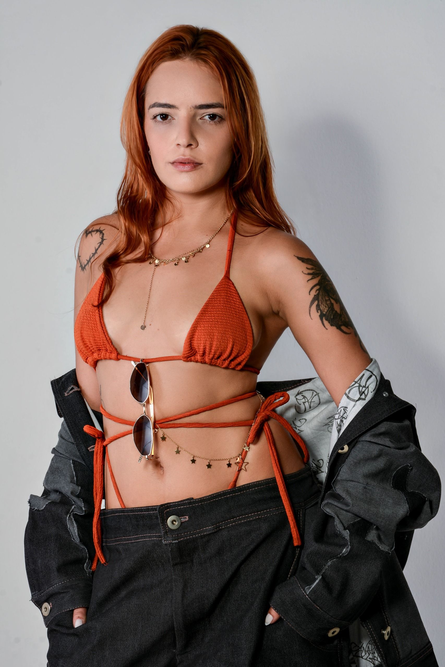 Mulher estilosa de biquíni laranja, jaqueta e joias posando com confiança.