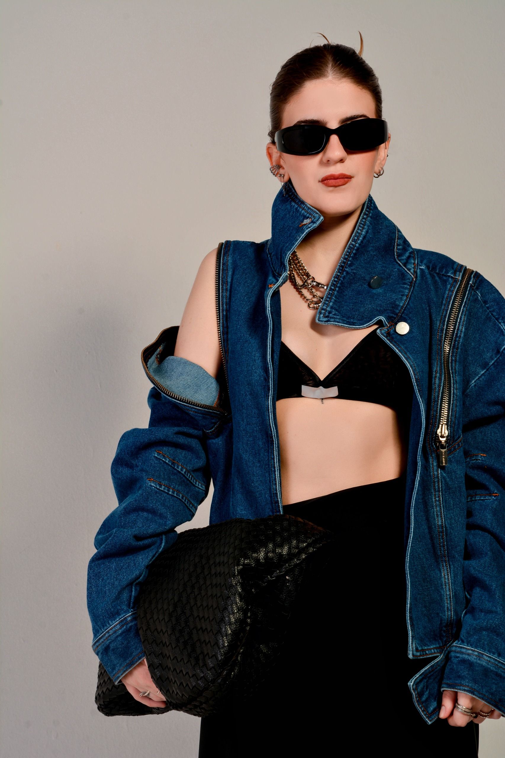 Uma mulher elegante vestindo uma jaqueta jeans e óculos de sol, segurando uma bolsa preta.
