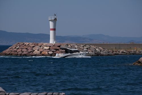 Free A scenic view of a lighthouse and motorboat at Foça harbor in İzmir, Türkiye. Stock Photo