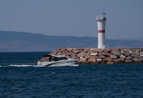 Free A boat sails past a lighthouse at the rocky shore in Foça, İzmir, Türkiye. Stock Photo