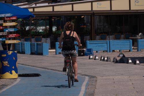 Free Rear view of a woman cycling on a coastal path in Foça, İzmir, Türkiye on a sunny day. Stock Photo