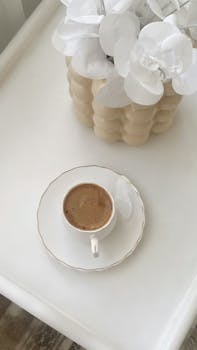 A minimalist scene with a coffee cup and decorative flowers on a chic white table.