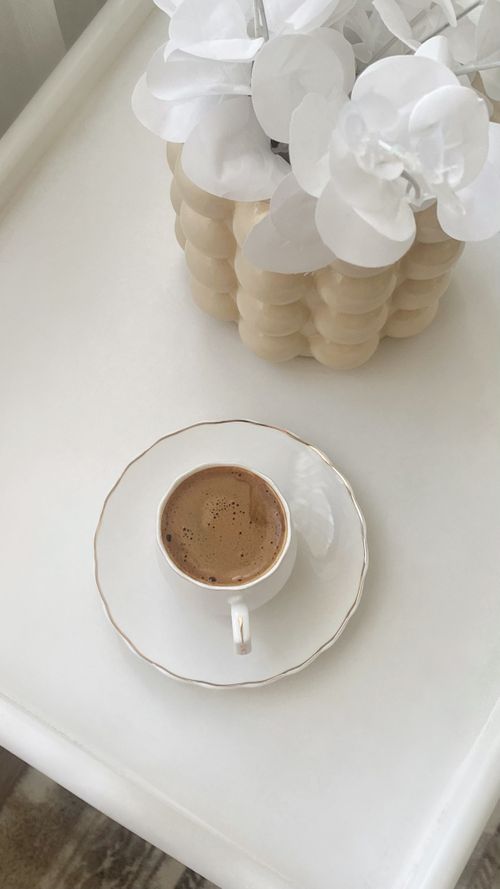 Free A minimalist scene with a coffee cup and decorative flowers on a chic white table. Stock Photo