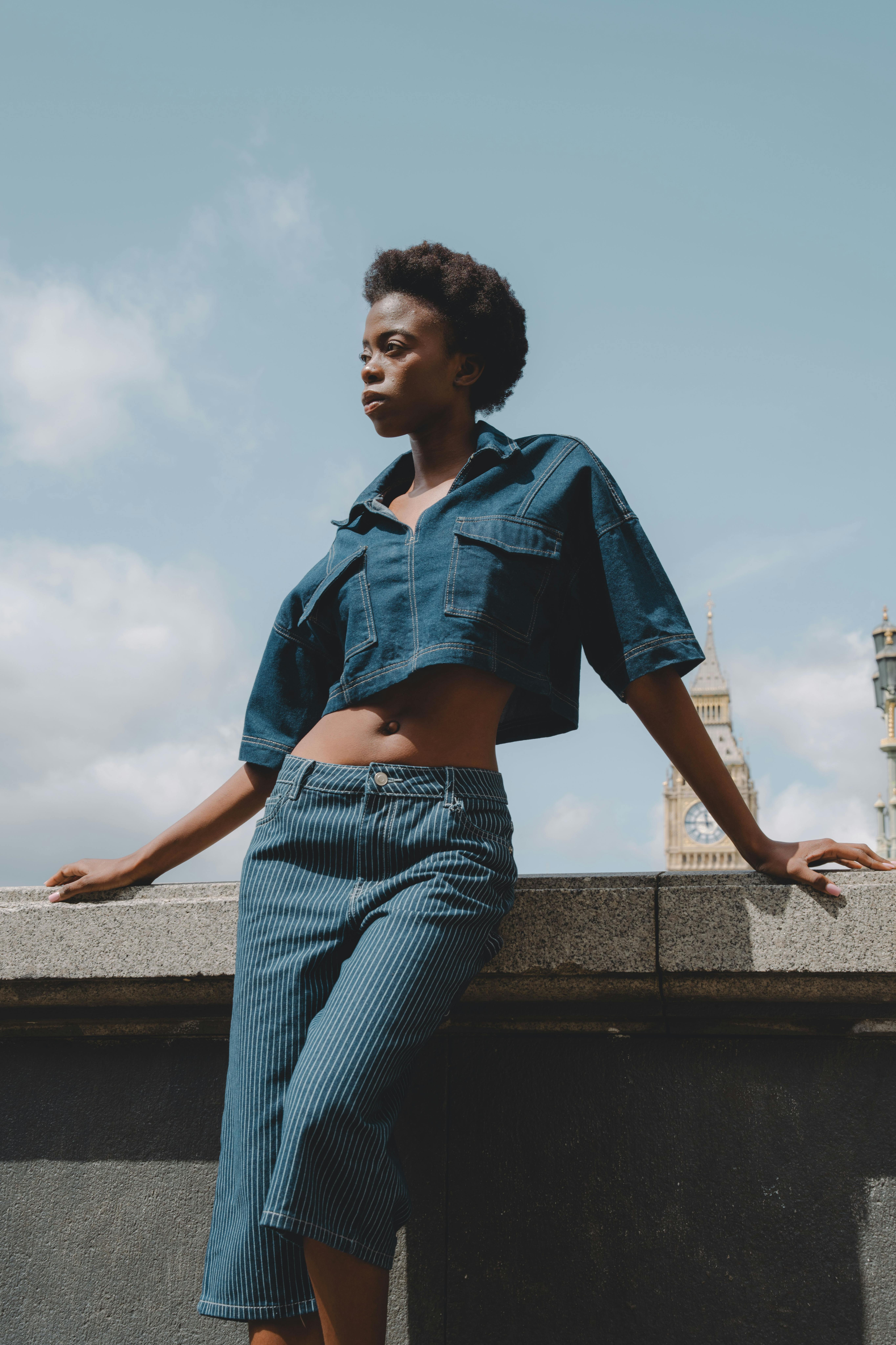 Confident woman in denim outfit posing outdoors with London skyline in the background.