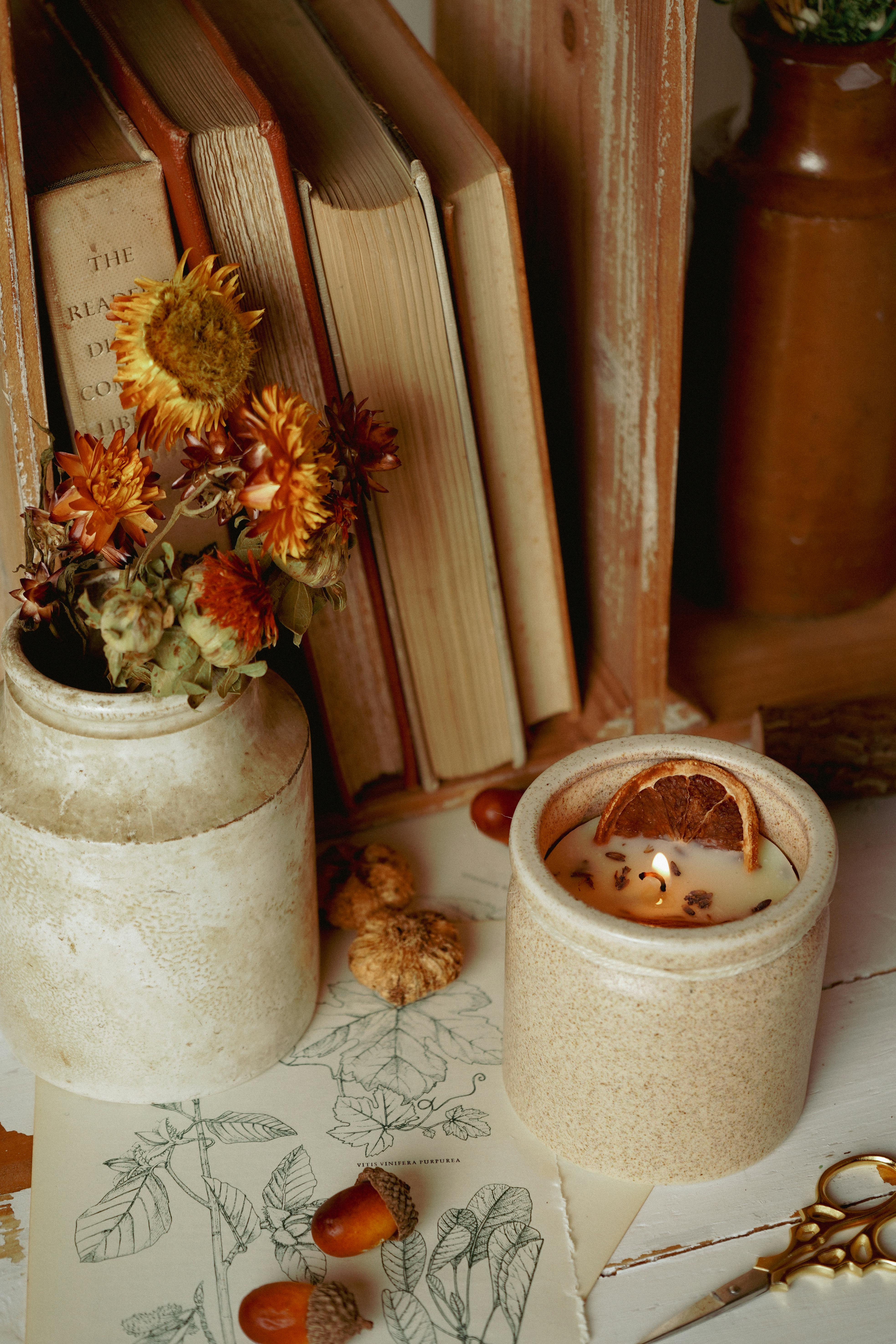A warm, autumn-inspired still life featuring vintage books, a lit candle, and dried flowers.