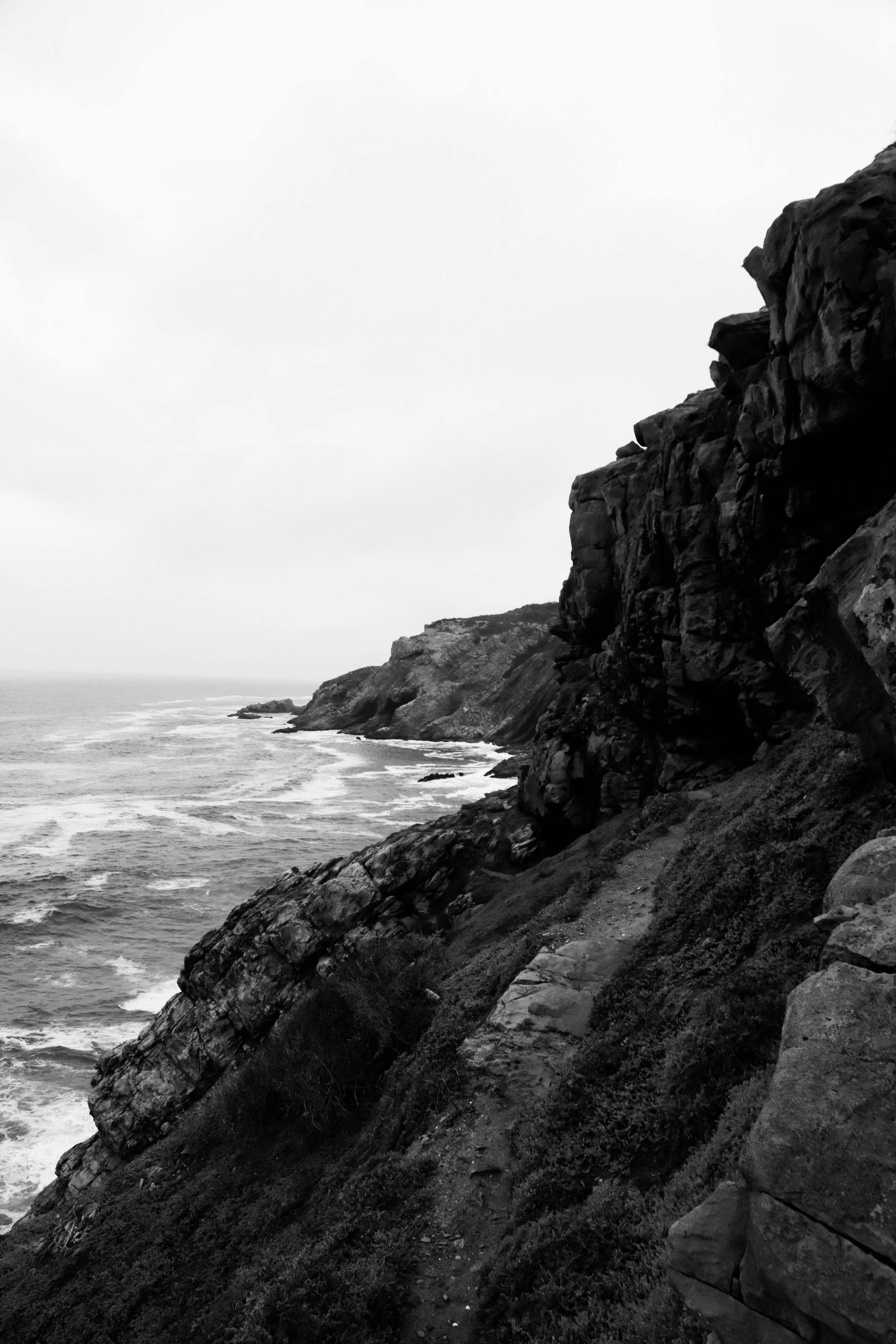 Monochrome view of jagged cliffs by a rugged coastline under an overcast sky.