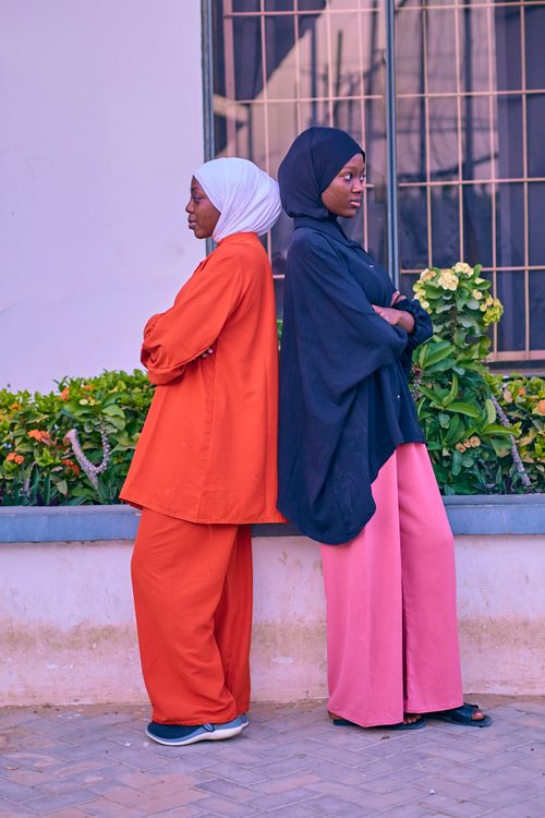Free Two women in colorful hijabs and outfits standing back to back outdoors. Stock Photo