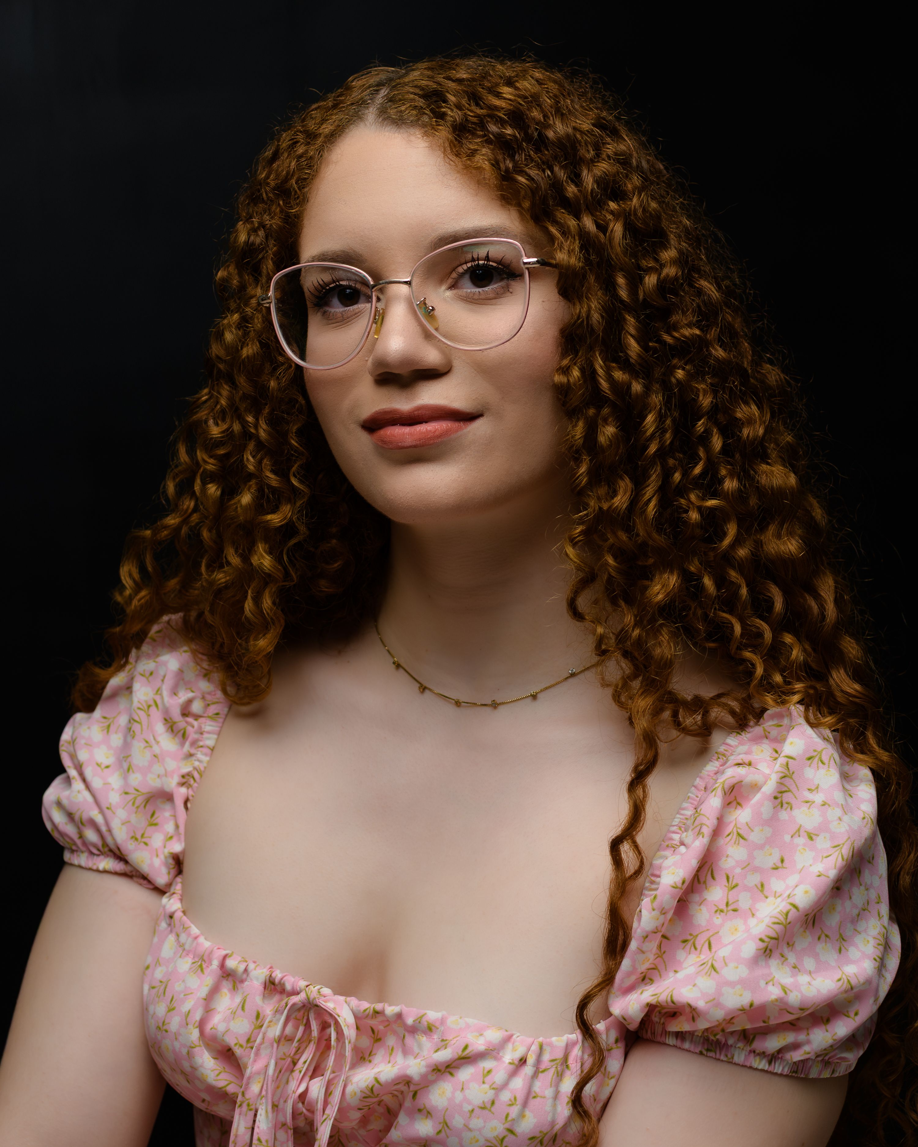 Elegant portrait of a woman with curly hair and glasses wearing a floral dress.
