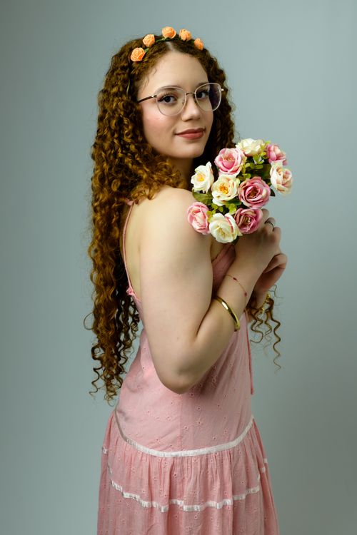 Free A woman in a pink dress holding a bouquet of delicate roses with a serene expression, embodying grace and femininity. Stock Photo