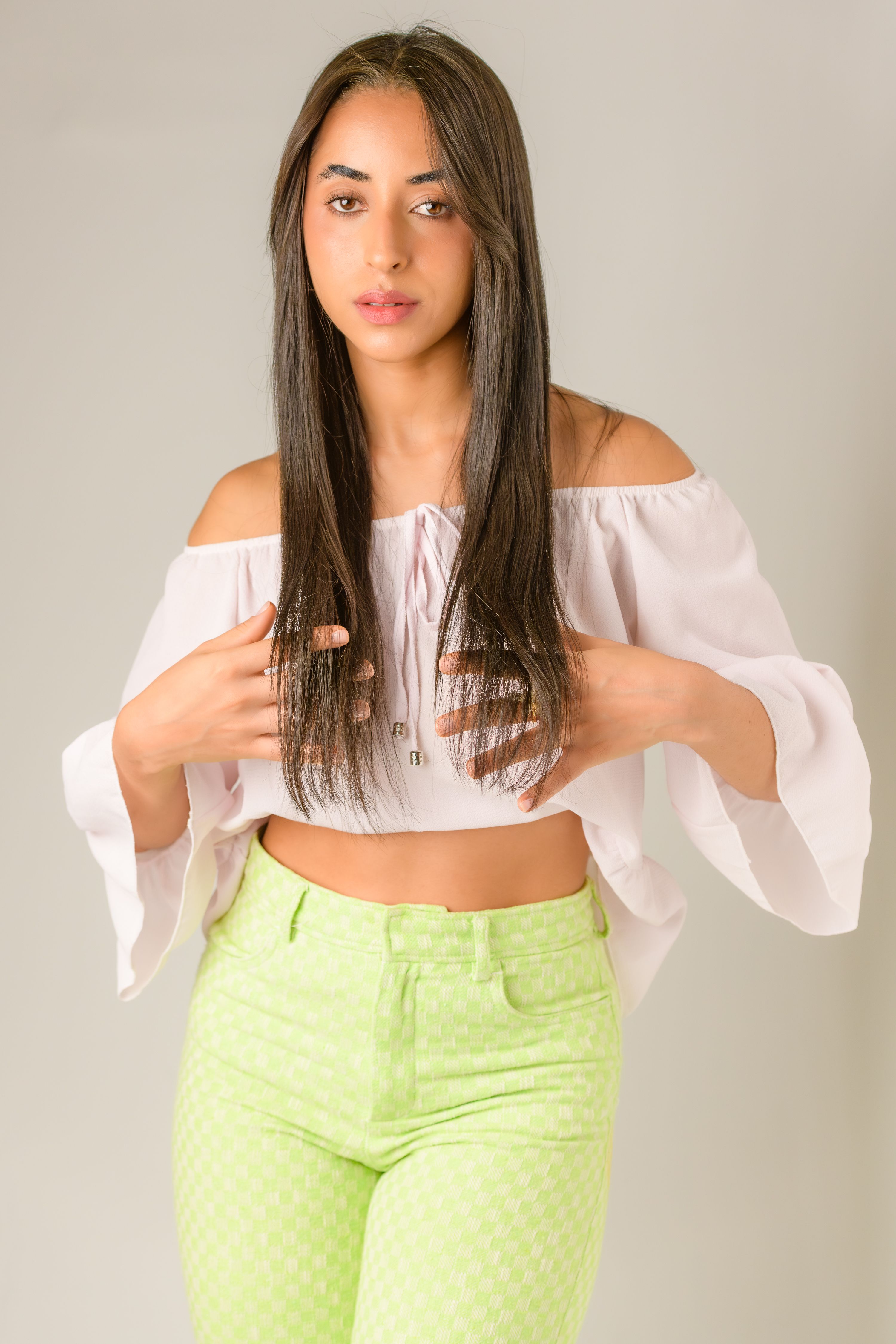Portrait of a young woman in a stylish off-shoulder top and vibrant pants in a studio setting.