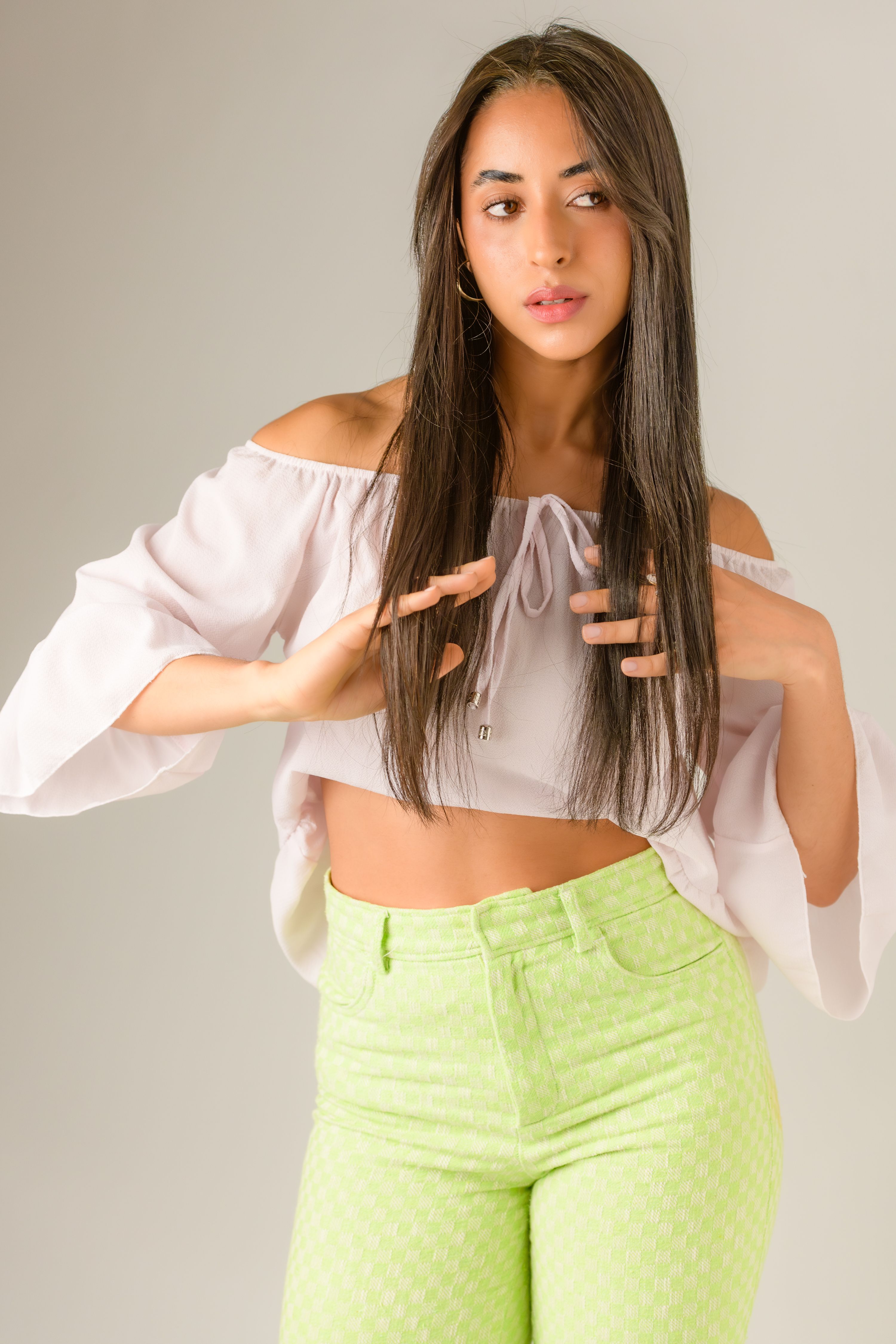 Fashionable young woman in a trendy off-shoulder top and bright pants striking a pose indoors.