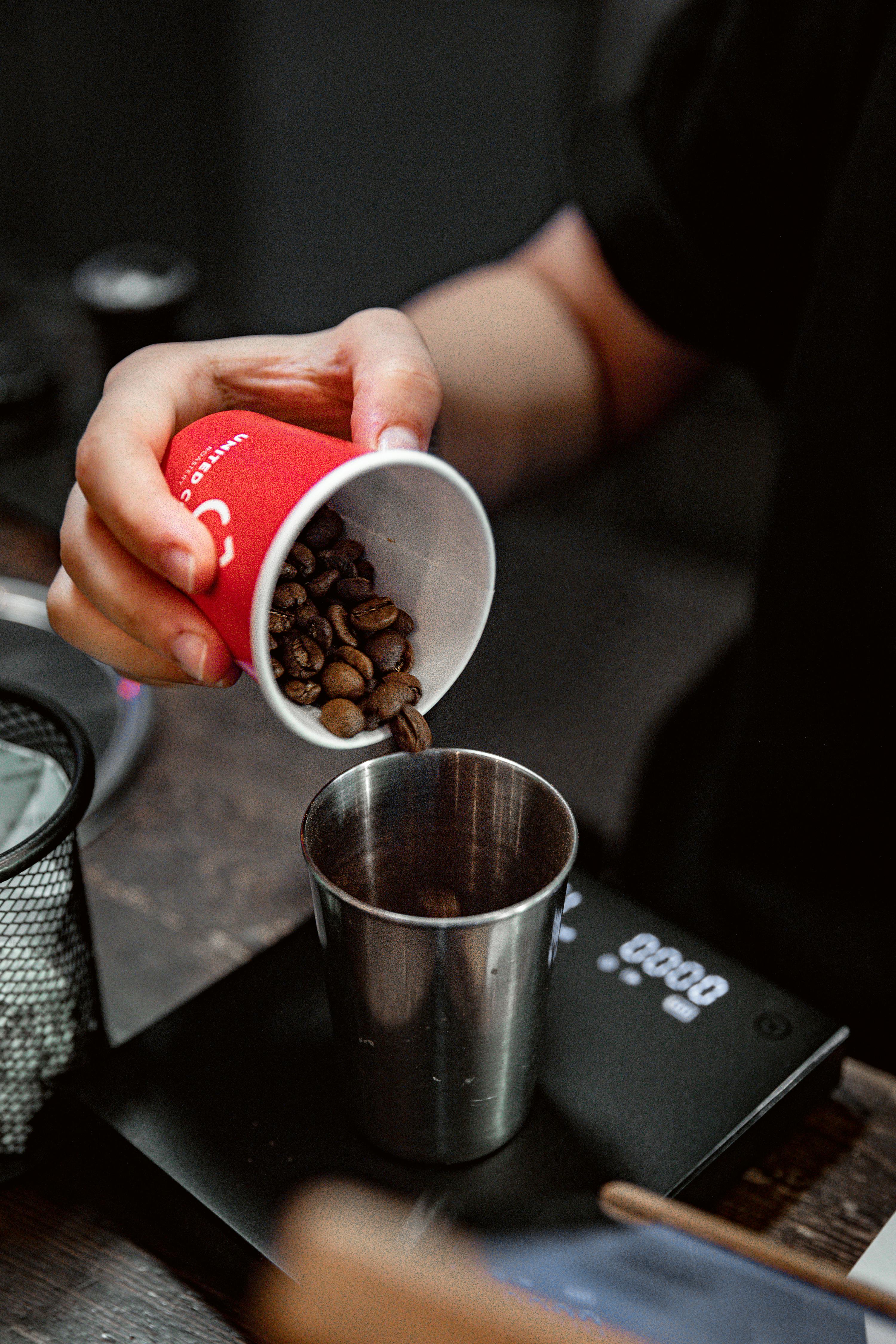 Close-up of hand pouring coffee beans into a cup on a scale at a Baku cafe.