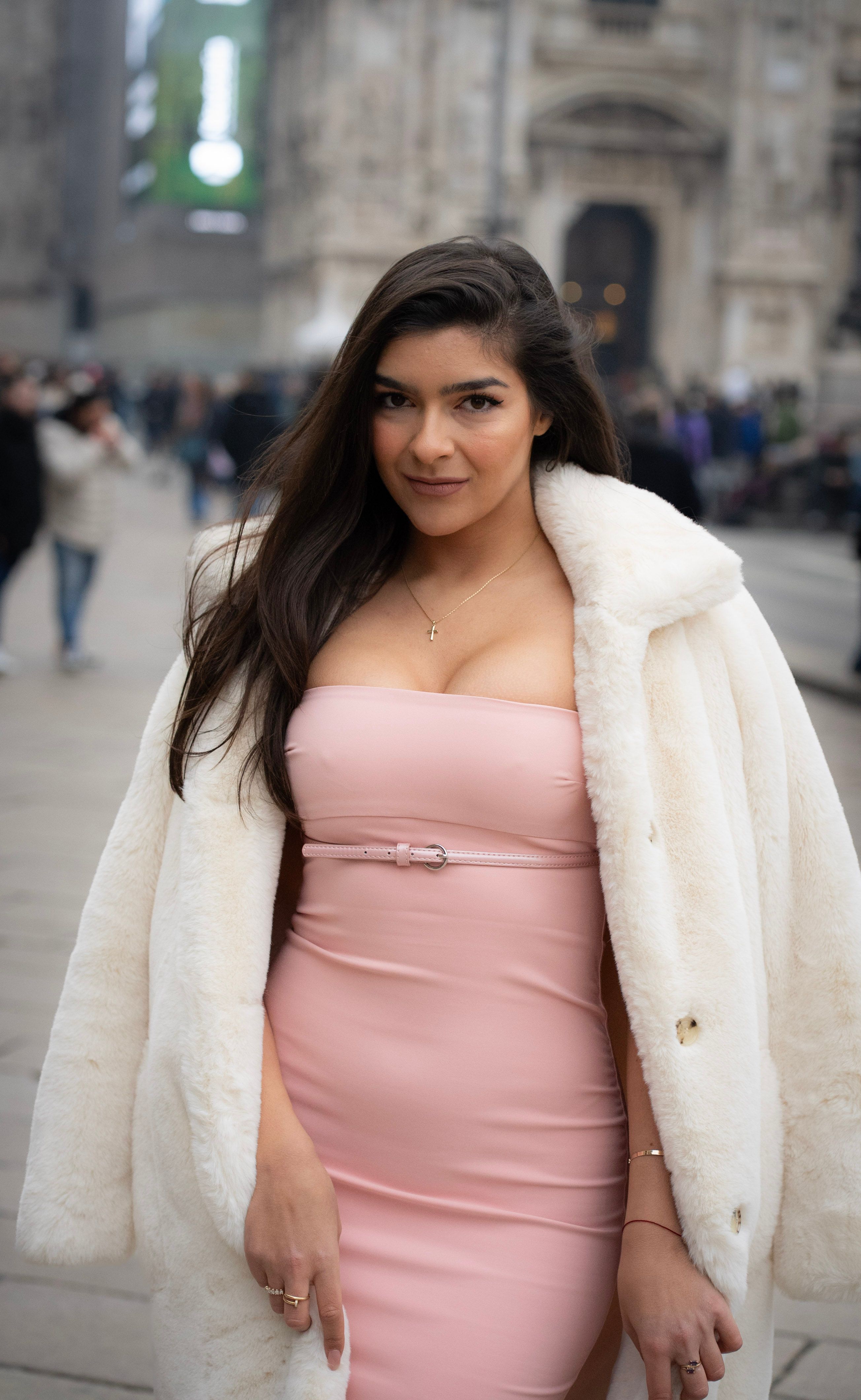 Beautiful young woman in pink dress and coat posing confidently in Milan's historic center.