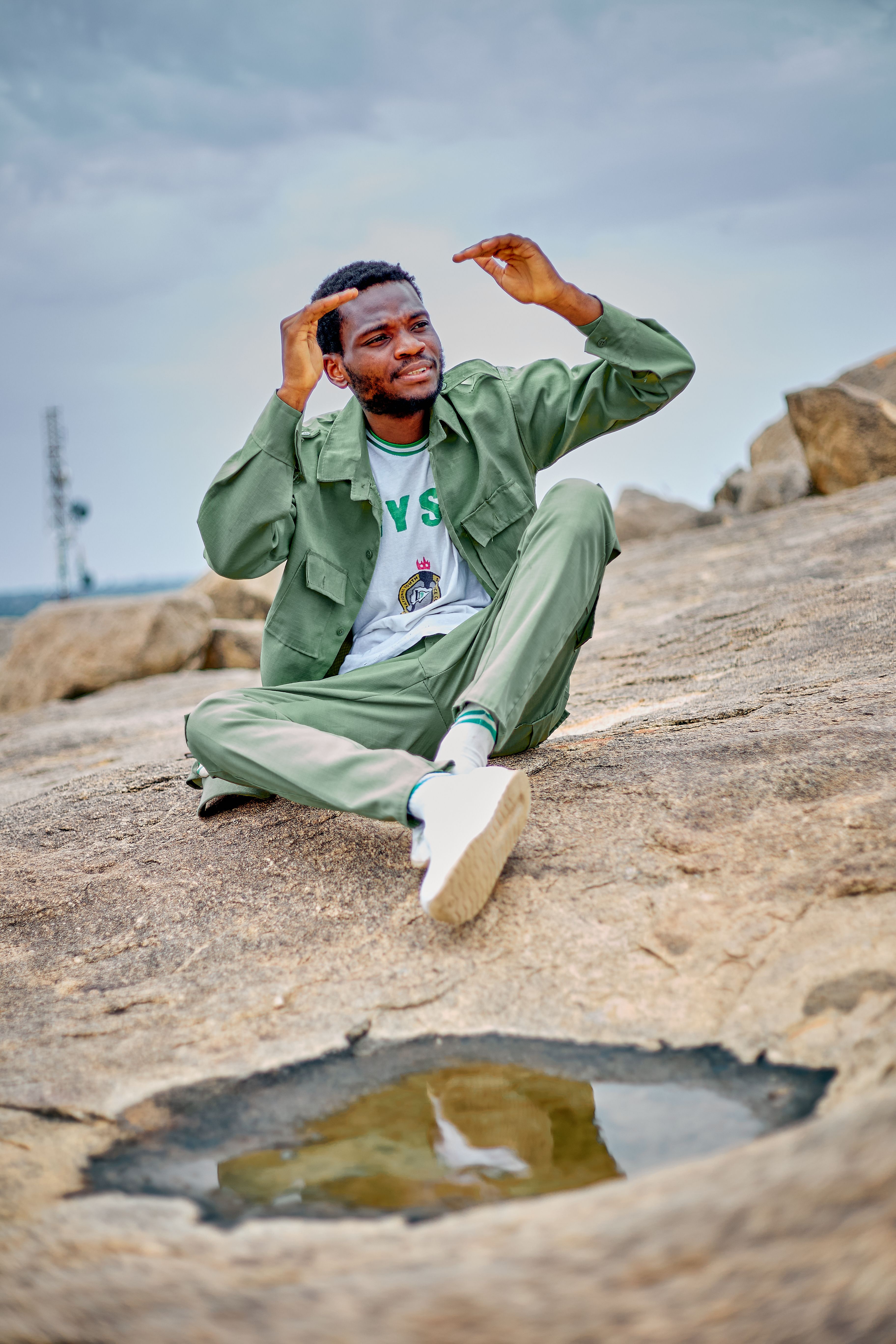 Casually dressed young man sits joyfully on rocky terrain, showcasing outdoor relaxation.