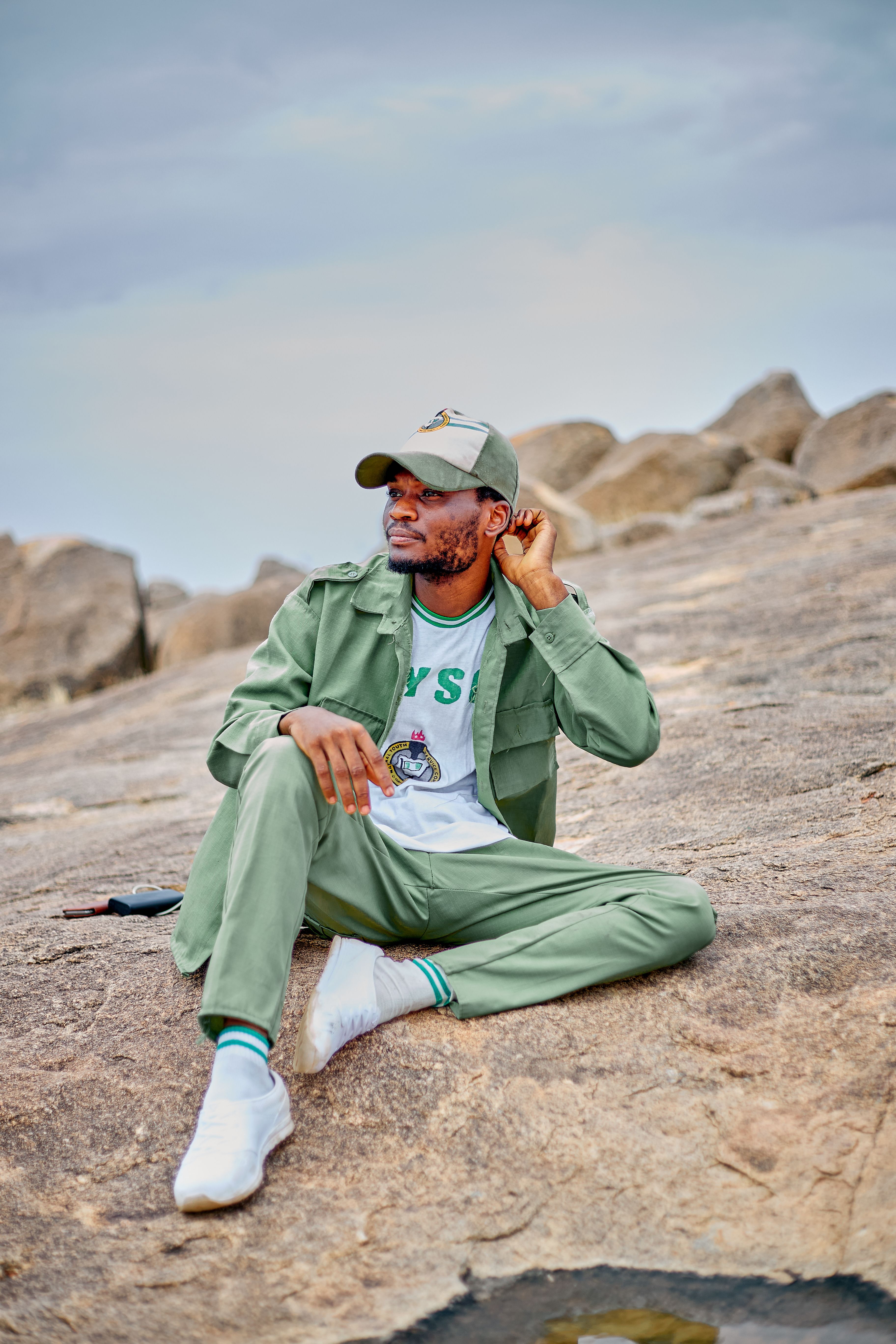 Casually dressed man sits on rocks outdoors, looking contemplative. Perfect for lifestyle and outdoor themes.