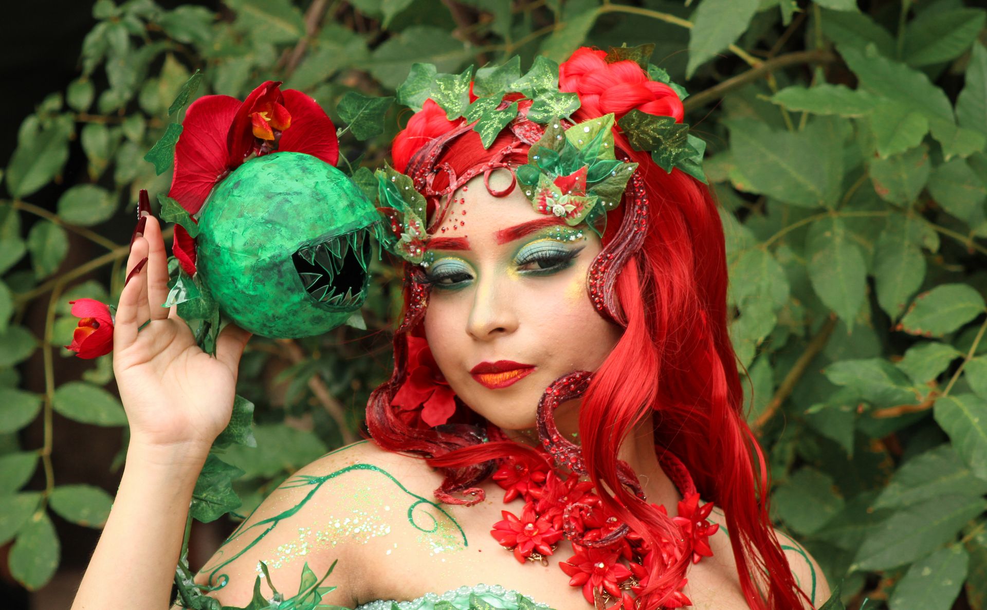 Vibrant cosplay featuring a woman in a nature-inspired villain costume with vivid red and green accents.