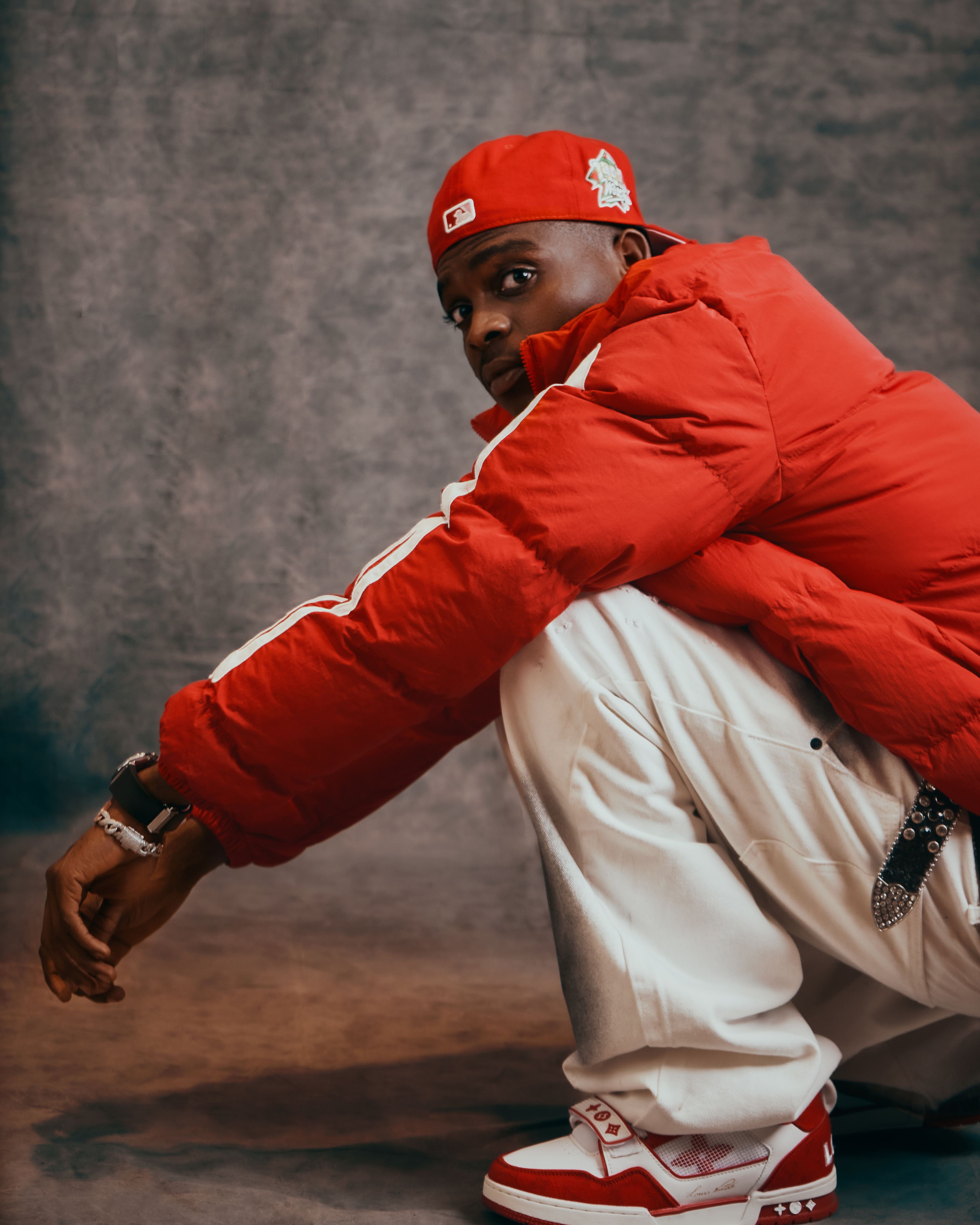 Man in a red jacket and cap squatting indoors in stylish attire. Fashionable and modern pose.
