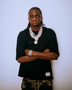 Young man posing confidently in black shirt and accessories, exuding an urban style.
