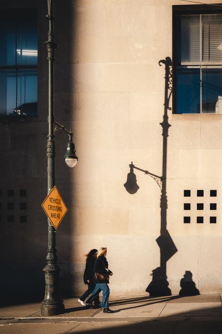 Silhouettes of two women walking along a wall in New York City, casting long shadows in the afternoon sun.
