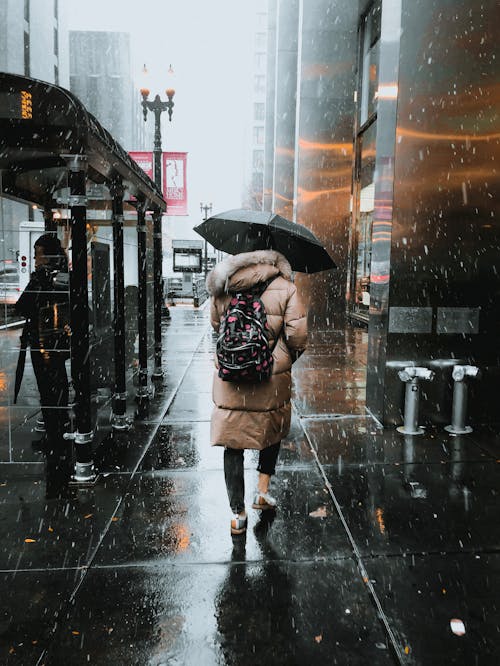 Женщина идет по улице под черным зонтом