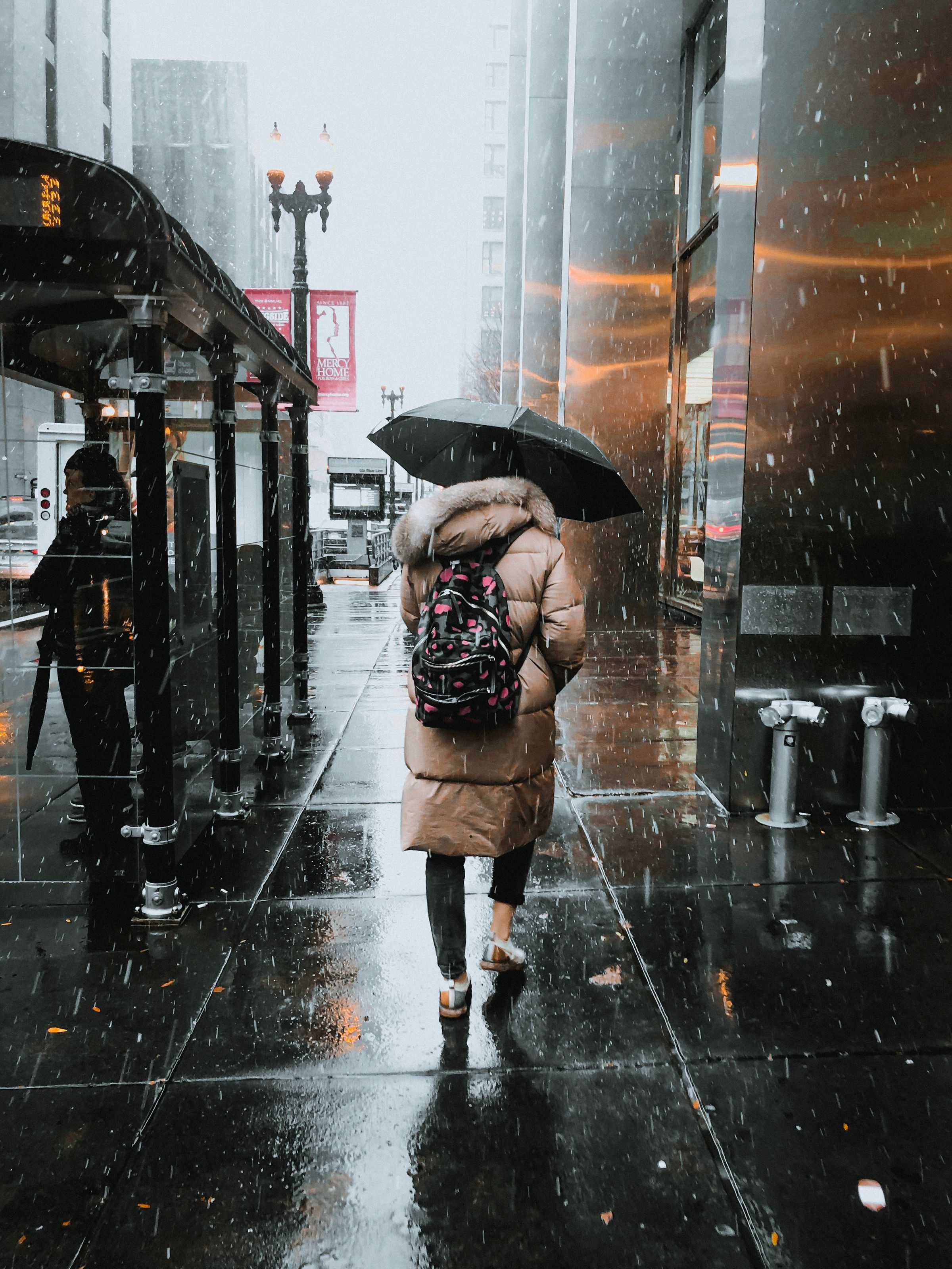 Woman walking on a wet city street under a black umbrella in cool rain