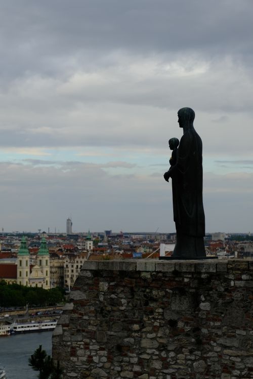 Free Silhouette of a statue on a stone wall with cityscape in the background. Stock Photo