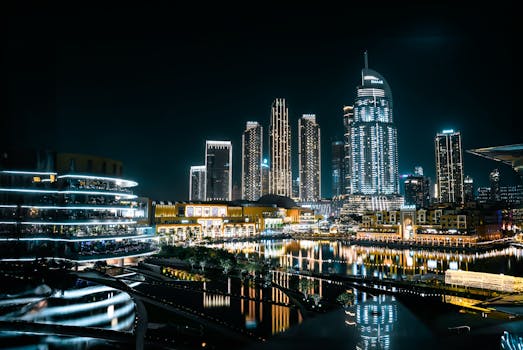 Vibrant cityscape of Dubai at night with illuminated skyscrapers reflecting on the waterfront.