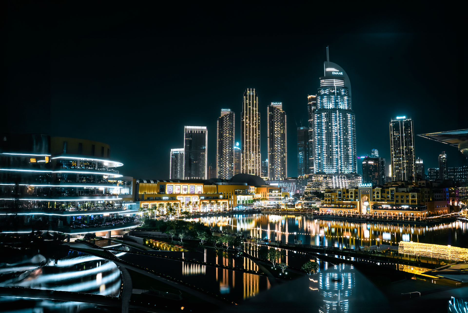 Vibrant cityscape of Dubai at night with illuminated skyscrapers reflecting on the waterfront.