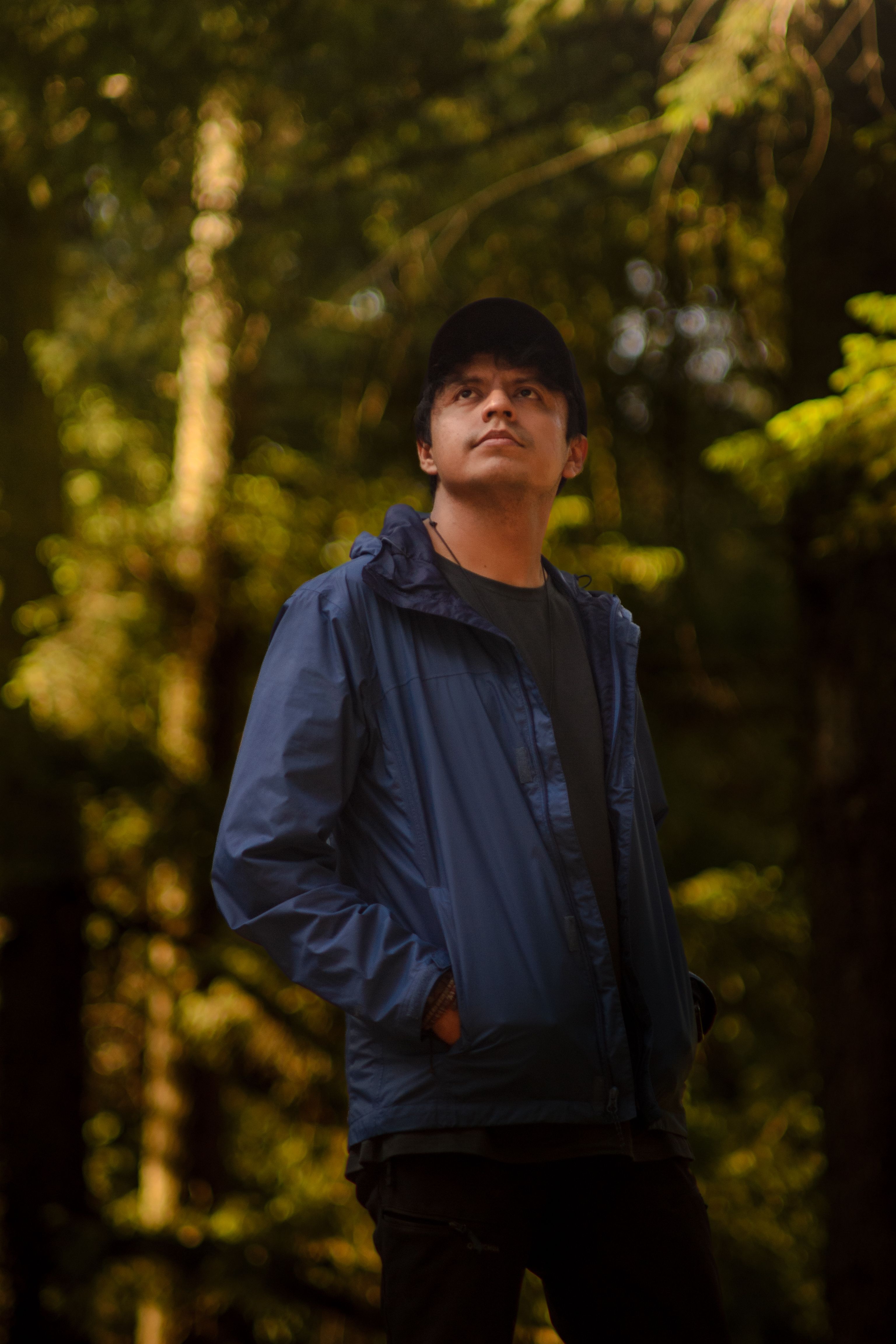 A young man in a blue jacket explores a sunlit forest in Mexico City.