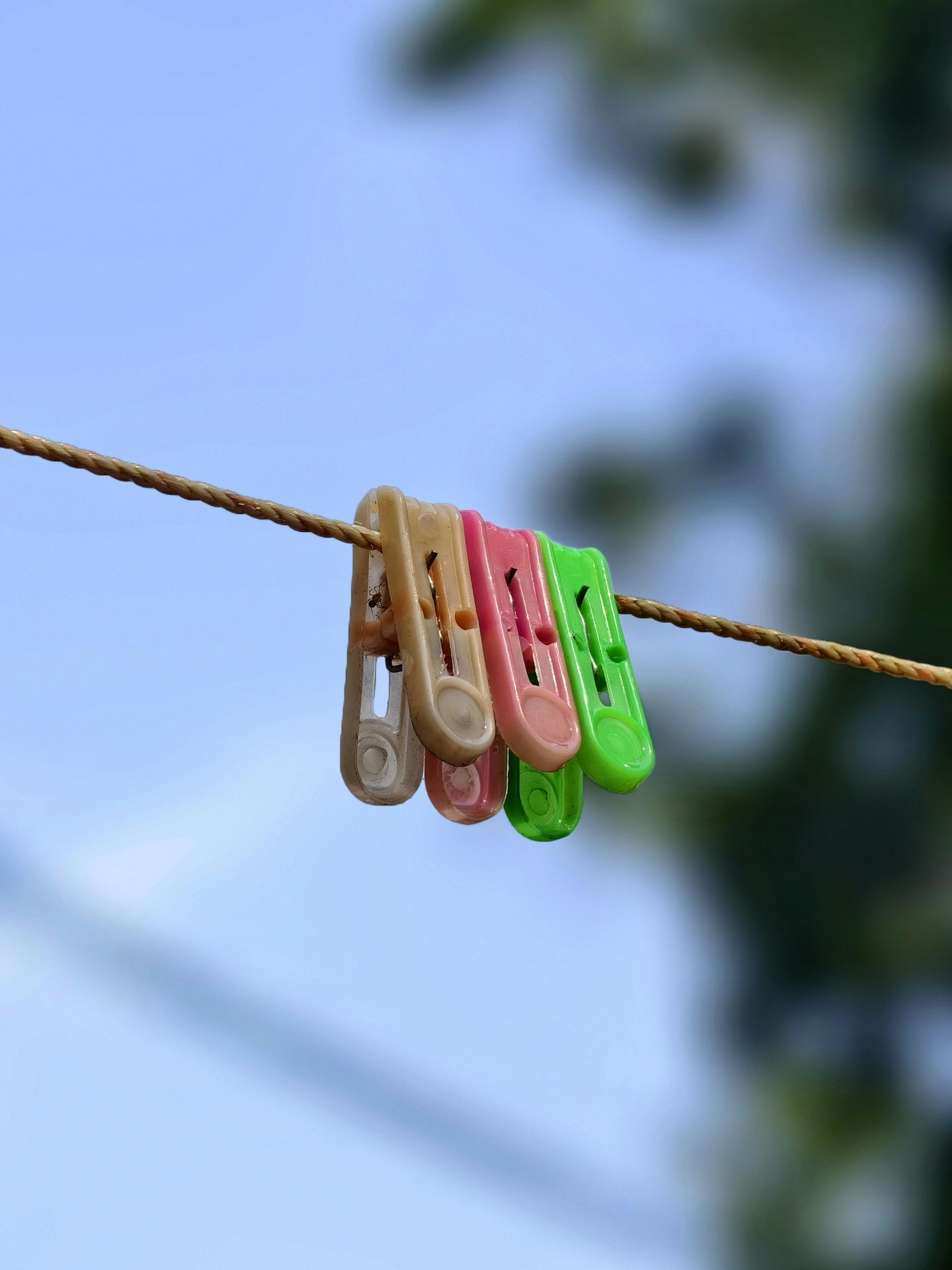 Gratis Et nærbilde av fargerike klesklyper på en ståltråd mot en klar blå himmel, som skaper en minimalistisk komposisjon. Arkivbilde