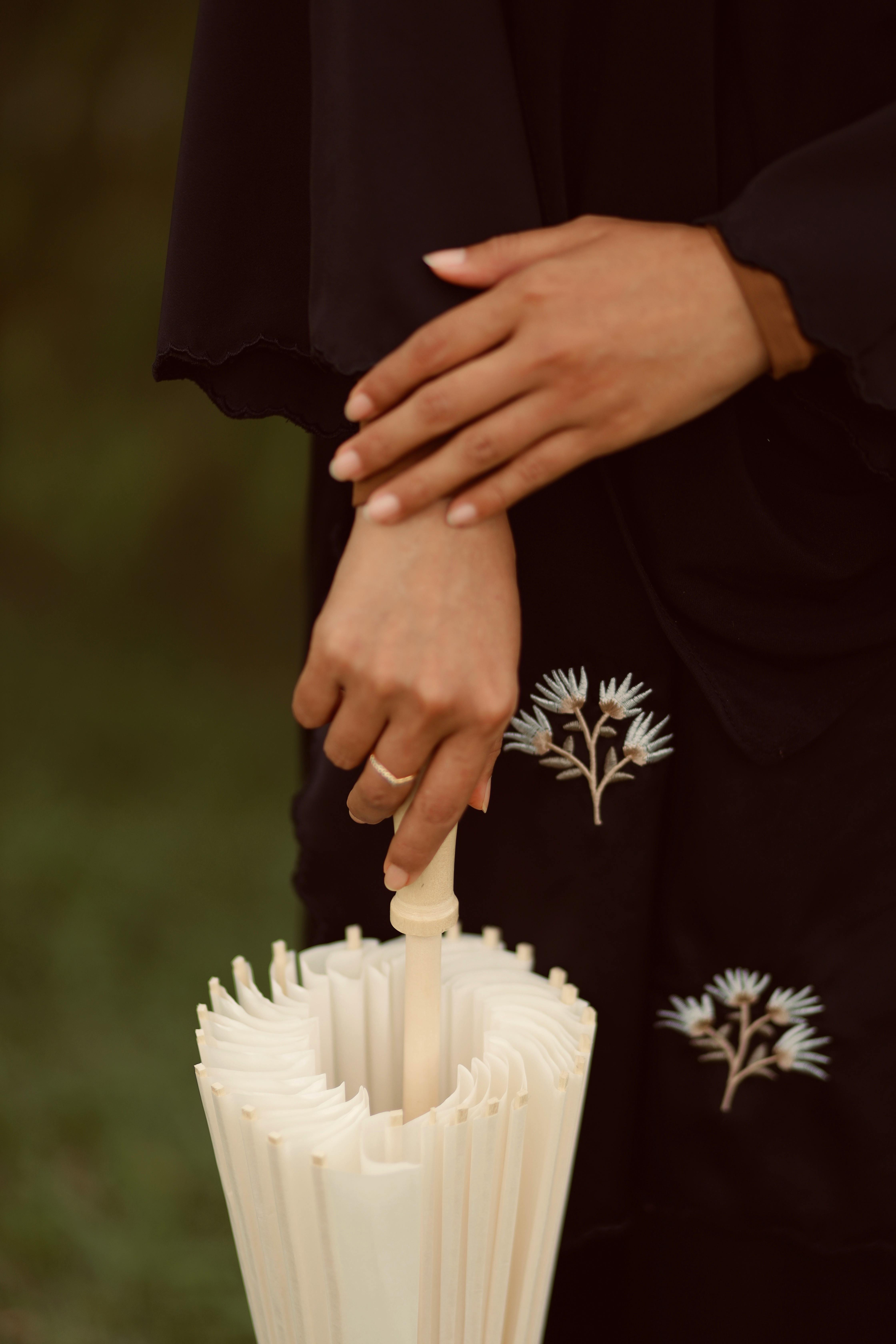Close-up of hands with a black floral dress holding a white umbrella outdoors.