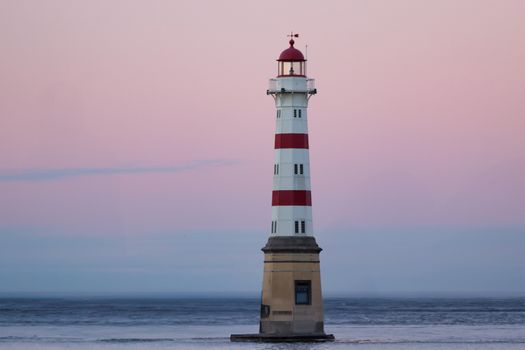 Captivating view of a lighthouse by the sea with a pink sunset sky in Rouen, Normandy, France.