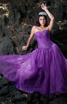 Woman in a stunning purple gown with a tiara posing against a natural rock backdrop.