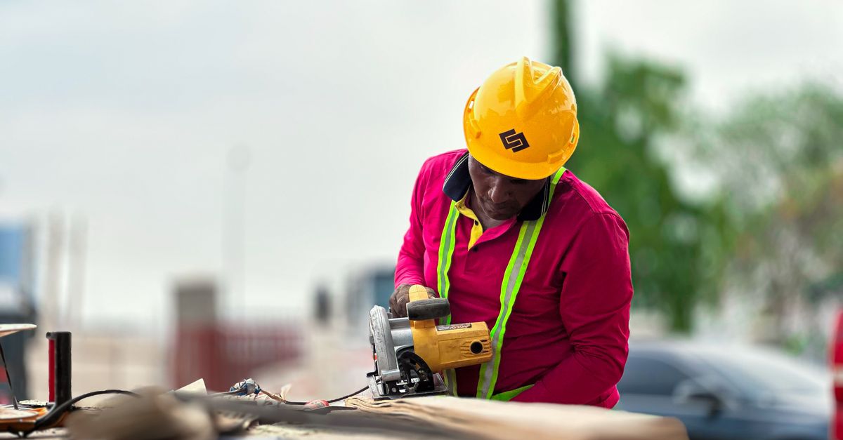 Construction worker wearing safety gear using an angle grinder on a site outdoors.