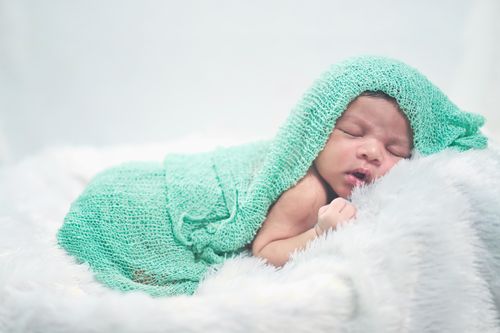 Free Serene image of a newborn baby wrapped in a soft green knit blanket, resting peacefully. Stock Photo