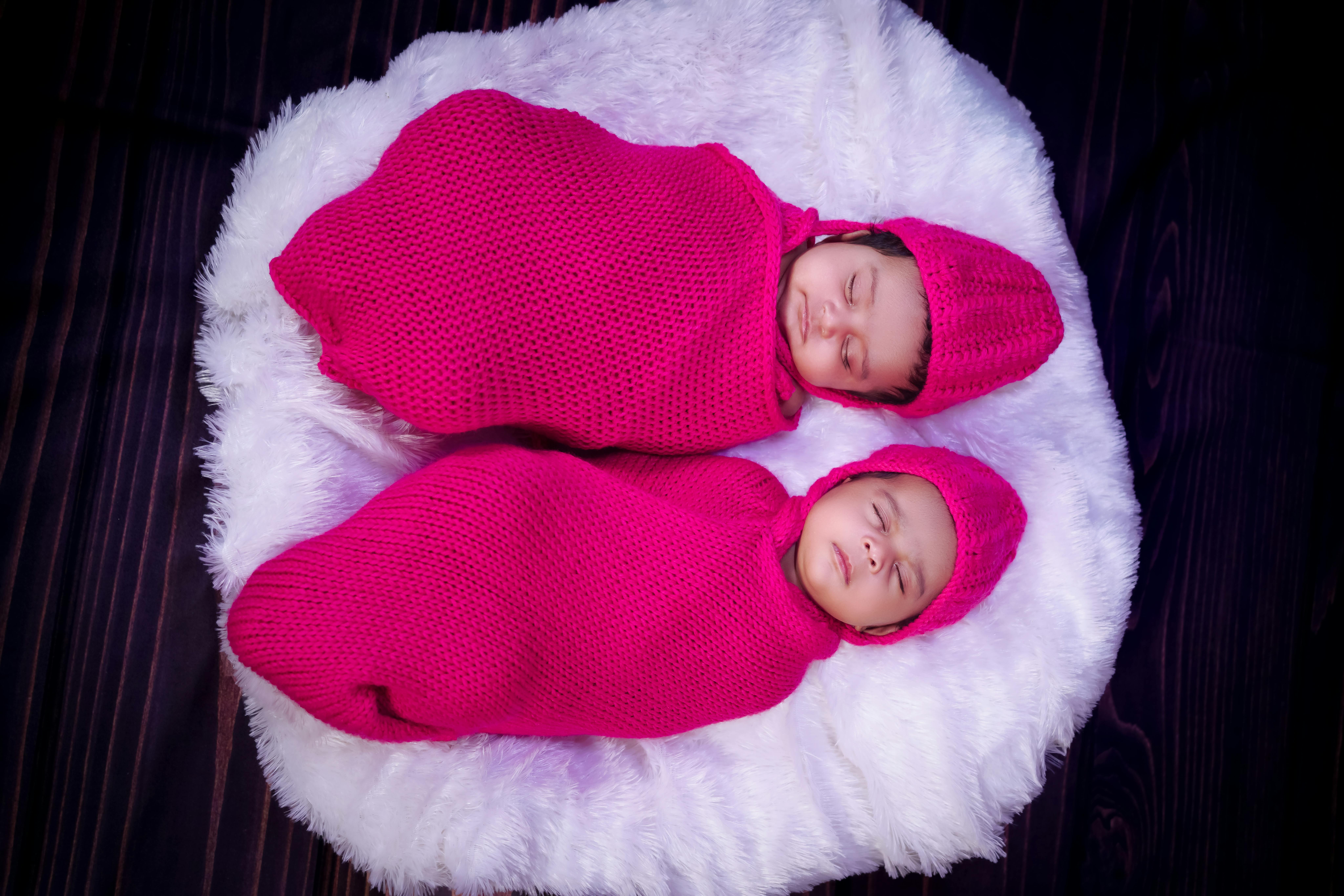 Charming image of twin babies peacefully sleeping in pink knit swaddles on a fluffy surface.